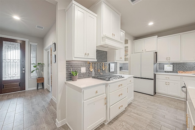 kitchen with white fridge, custom exhaust hood, light wood-type flooring, white cabinets, and stainless steel gas stovetop