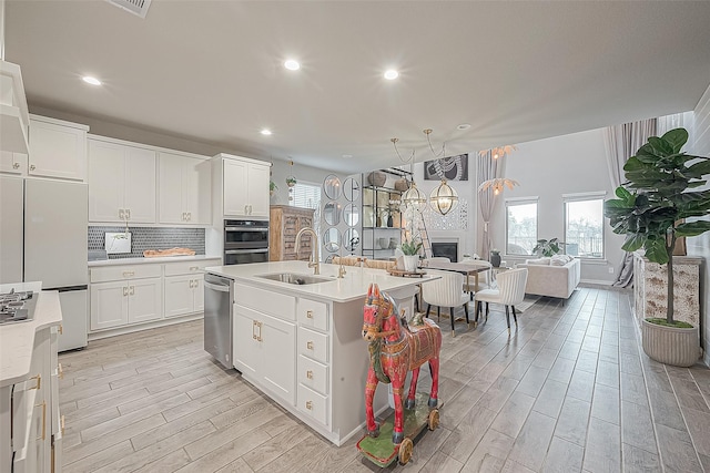 kitchen featuring white cabinetry, a kitchen island with sink, white refrigerator, sink, and dishwasher