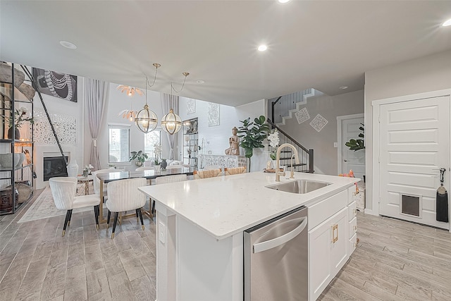 kitchen featuring sink, decorative light fixtures, stainless steel dishwasher, white cabinets, and an island with sink