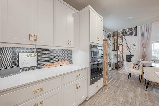 kitchen with decorative backsplash, light stone countertops, white cabinets, and black double oven