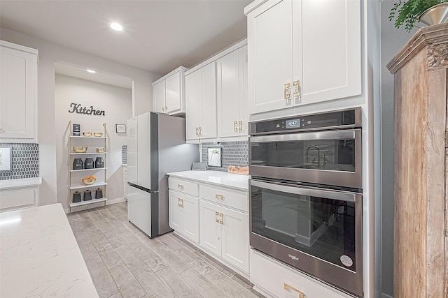 kitchen with light wood-type flooring, appliances with stainless steel finishes, white cabinets, and decorative backsplash