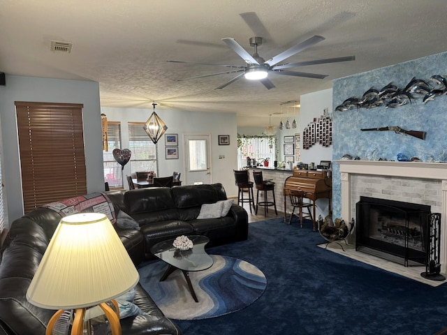 carpeted living room with ceiling fan with notable chandelier, a large fireplace, and a textured ceiling