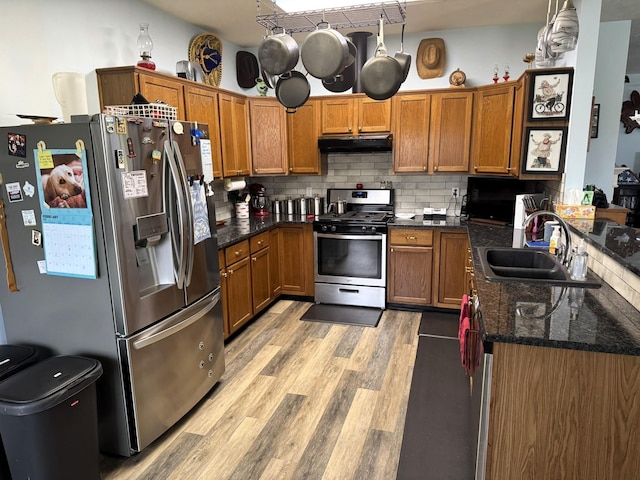 kitchen featuring dark stone countertops, appliances with stainless steel finishes, sink, light hardwood / wood-style floors, and hanging light fixtures