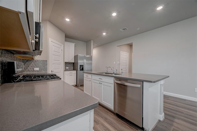 kitchen featuring appliances with stainless steel finishes, a center island with sink, backsplash, sink, and white cabinetry