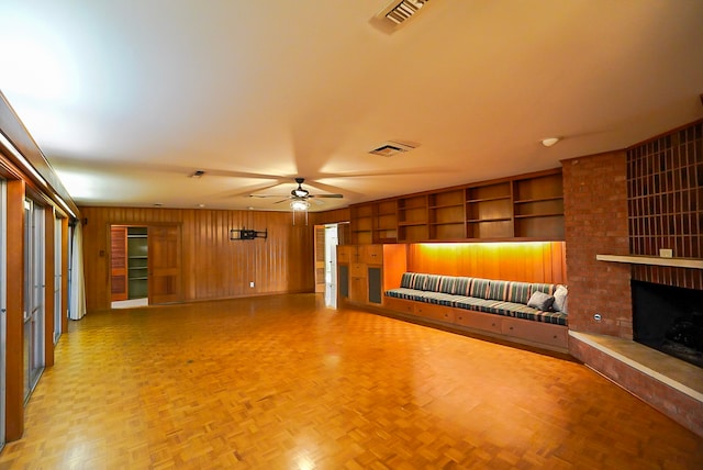 unfurnished living room featuring a brick fireplace, built in shelves, parquet floors, ceiling fan, and wooden walls