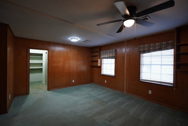 spare room featuring ceiling fan, carpet flooring, and wood walls