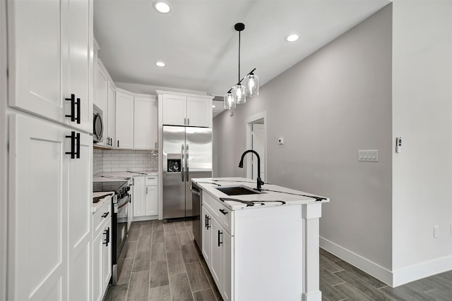 kitchen with appliances with stainless steel finishes, white cabinets, backsplash, sink, and a kitchen island with sink