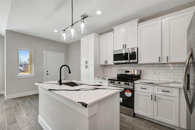 kitchen with white cabinetry, stainless steel appliances, pendant lighting, and a kitchen island with sink