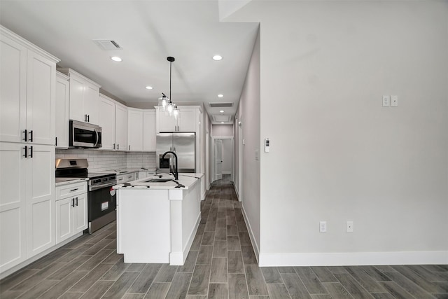 kitchen featuring appliances with stainless steel finishes, white cabinets, pendant lighting, backsplash, and a kitchen island with sink