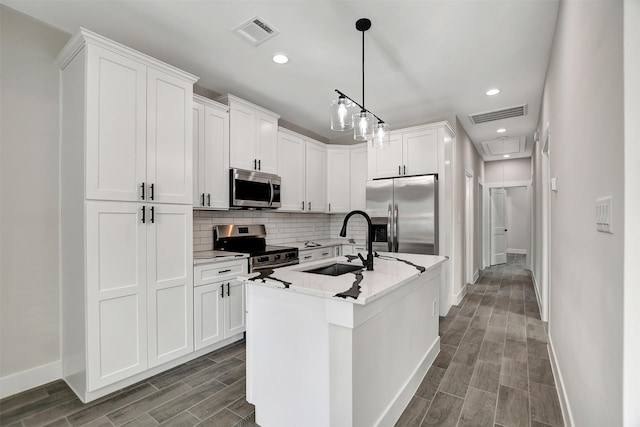 kitchen featuring a kitchen island with sink, decorative light fixtures, tasteful backsplash, appliances with stainless steel finishes, and white cabinets