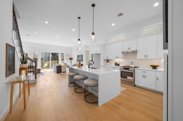 kitchen featuring a center island with sink, gas range, decorative light fixtures, light countertops, and white cabinetry