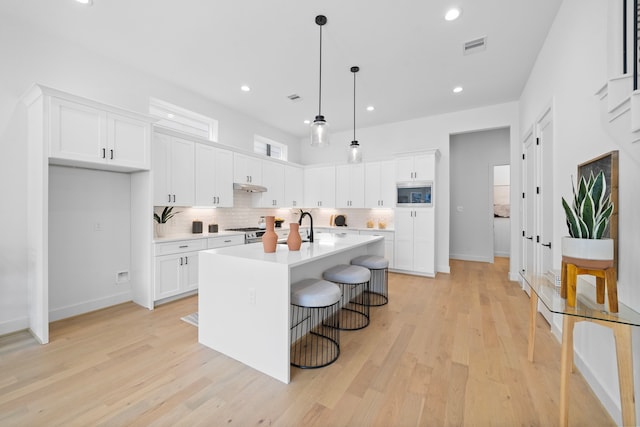 kitchen featuring white cabinetry, light countertops, hanging light fixtures, built in microwave, and an island with sink