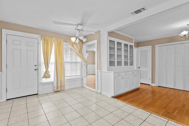 entryway featuring light tile patterned flooring, crown molding, and ceiling fan with notable chandelier