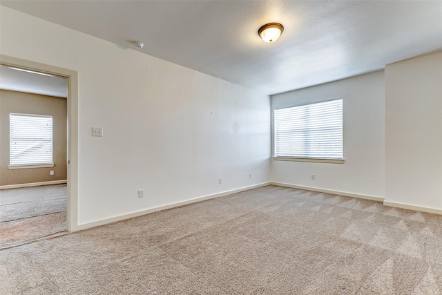 spare room featuring light carpet and baseboards