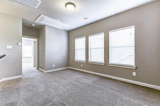 carpeted spare room with visible vents, attic access, and baseboards