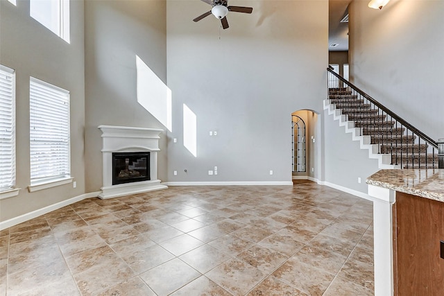 unfurnished living room with arched walkways, a glass covered fireplace, ceiling fan, baseboards, and stairs