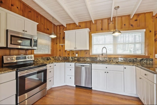 kitchen with white cabinetry, hanging light fixtures, wooden walls, and stainless steel appliances