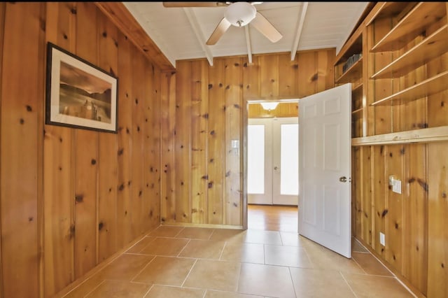 empty room featuring french doors, wood walls, ceiling fan, light tile patterned floors, and beamed ceiling