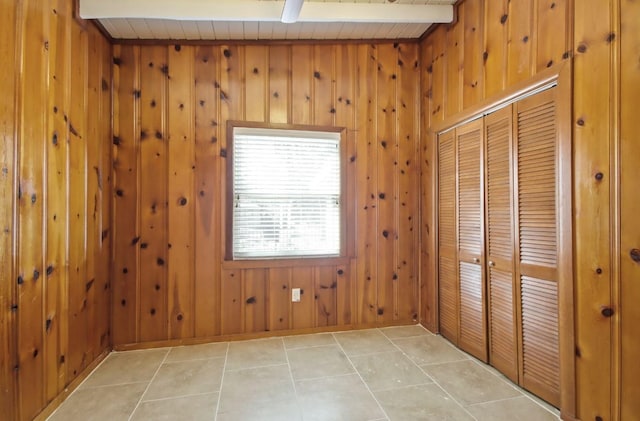 tiled empty room featuring beamed ceiling and wood walls