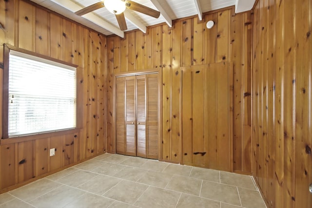 tiled empty room featuring ceiling fan, wood walls, and beam ceiling