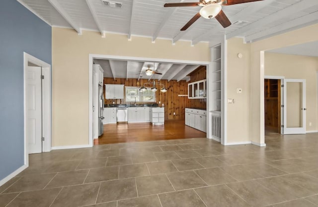 unfurnished living room featuring sink, wooden walls, ceiling fan, and beam ceiling