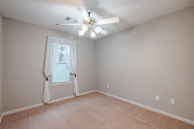 spare room featuring light carpet, visible vents, a ceiling fan, and baseboards