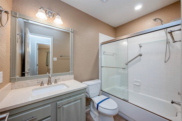 full bath with toilet, a textured wall, combined bath / shower with glass door, and vanity