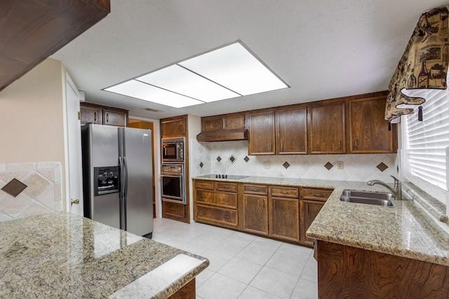 kitchen with decorative backsplash, under cabinet range hood, black appliances, a sink, and light tile patterned flooring