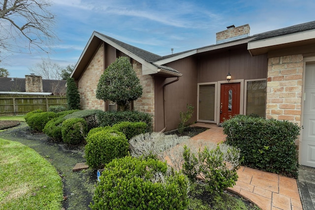 doorway to property featuring stone siding, a chimney, and fence