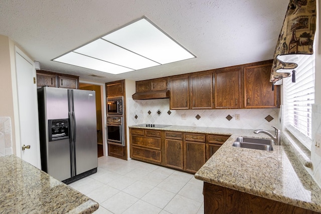 kitchen with light stone counters, under cabinet range hood, a sink, black appliances, and tasteful backsplash