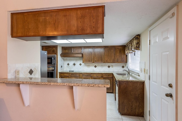 kitchen with brown cabinets, a sink, a peninsula, and black appliances