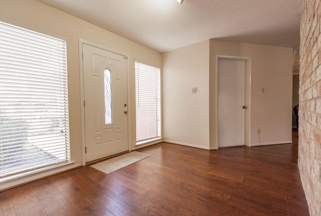 foyer entrance featuring a textured ceiling, dark wood finished floors, and baseboards