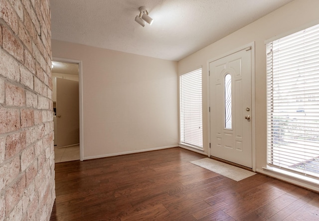 foyer entrance with dark wood-type flooring, a textured ceiling, and baseboards