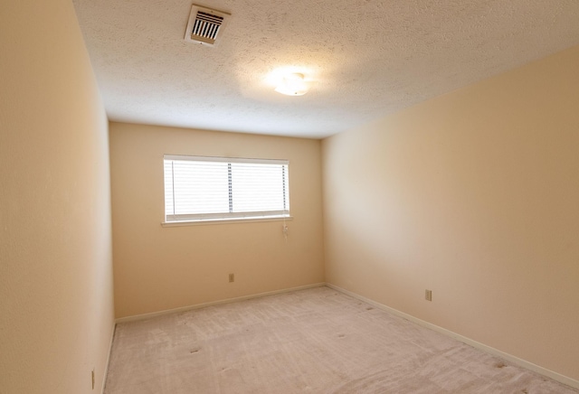 empty room with light colored carpet, visible vents, a textured ceiling, and baseboards