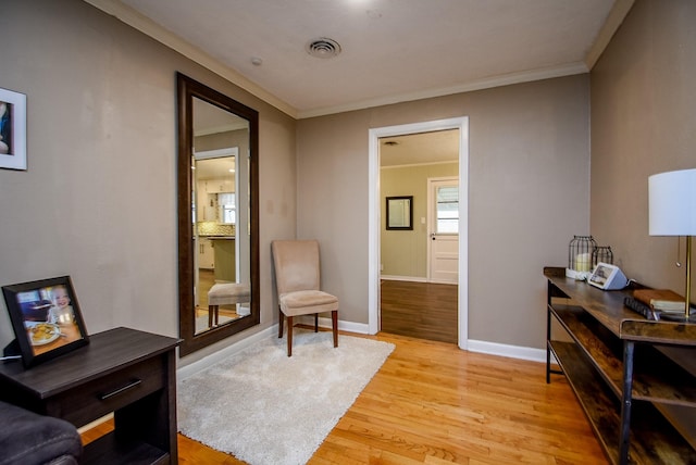 living area with baseboards, visible vents, light wood-type flooring, and ornamental molding