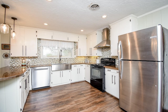 kitchen with wall chimney range hood, visible vents, a sink, dark wood-type flooring, and appliances with stainless steel finishes
