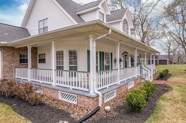 view of side of property with a shingled roof, covered porch, and brick siding