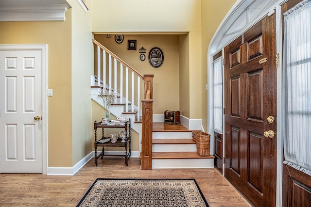 entryway featuring crown molding, stairway, light wood-style flooring, and baseboards