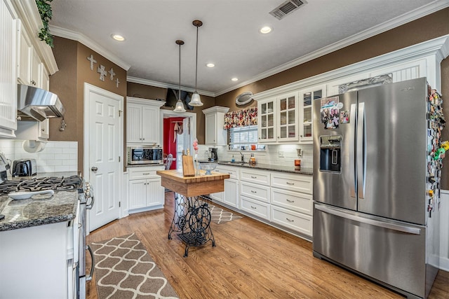 kitchen featuring extractor fan, decorative light fixtures, stainless steel appliances, visible vents, and glass insert cabinets