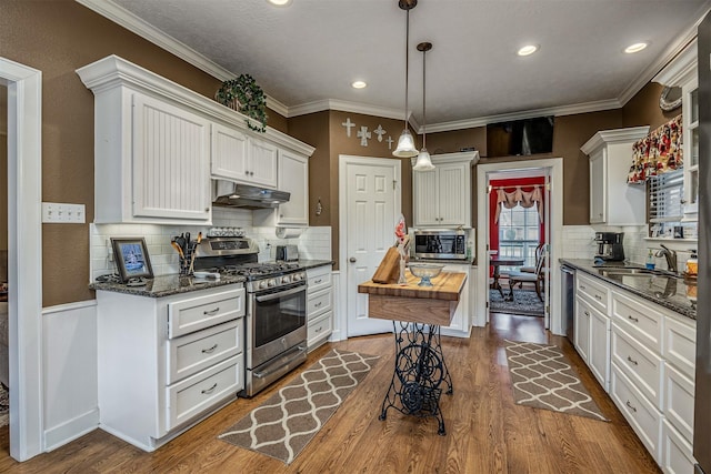 kitchen featuring decorative light fixtures, stainless steel appliances, under cabinet range hood, white cabinetry, and wooden counters