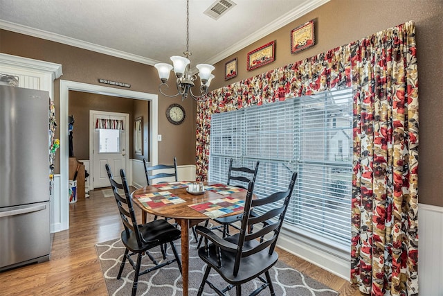 dining space with ornamental molding, a chandelier, visible vents, and wood finished floors