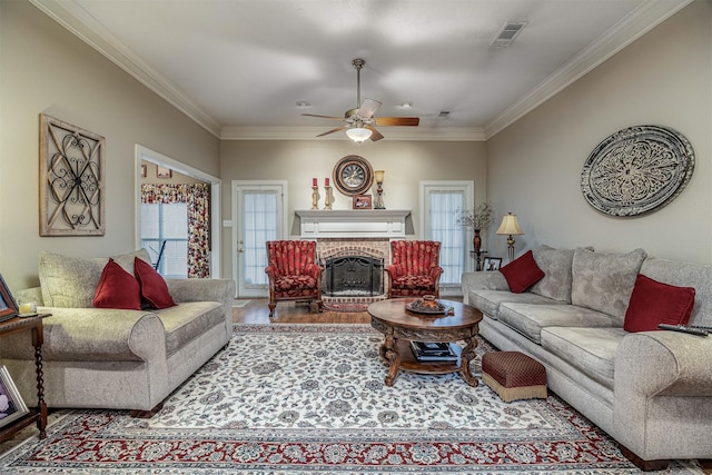 living room with crown molding, a fireplace, visible vents, ceiling fan, and wood finished floors