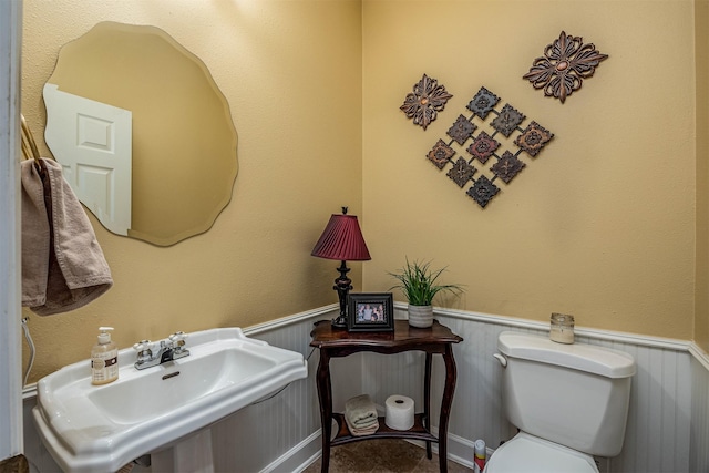 half bathroom featuring toilet, a wainscoted wall, and a sink