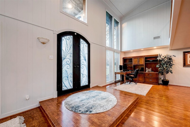 foyer entrance featuring visible vents, arched walkways, wood finished floors, french doors, and high vaulted ceiling