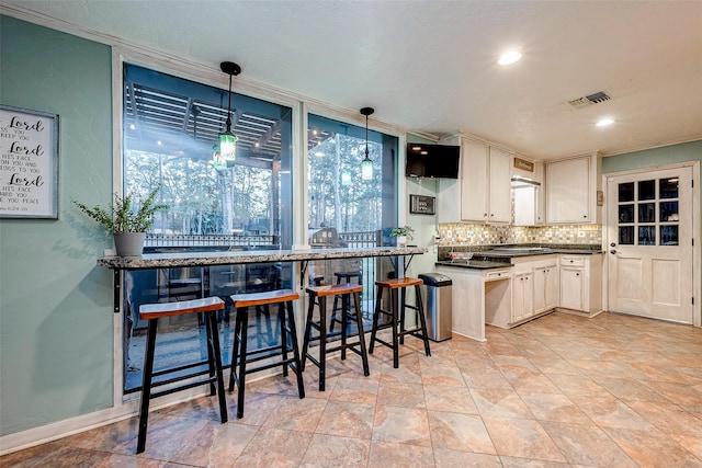 kitchen with tasteful backsplash, hanging light fixtures, stone finish floor, dark countertops, and visible vents