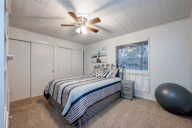bedroom featuring a ceiling fan, carpet floors, two closets, and a decorative wall
