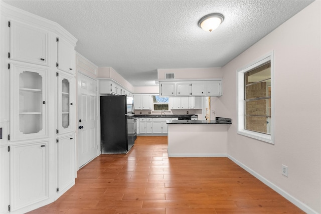 kitchen with light wood-type flooring, white cabinetry, black fridge, a textured ceiling, and kitchen peninsula