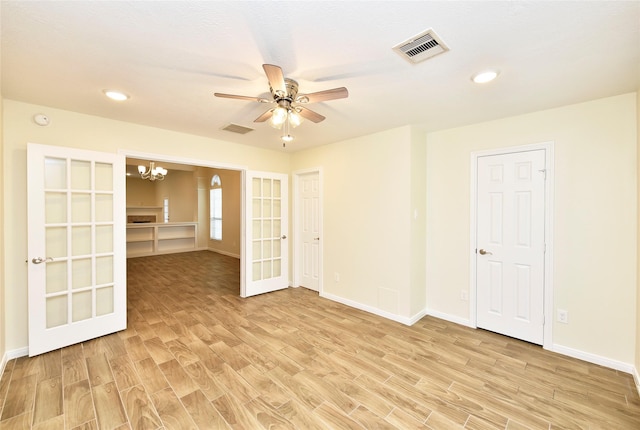 unfurnished room featuring ceiling fan with notable chandelier and light hardwood / wood-style flooring