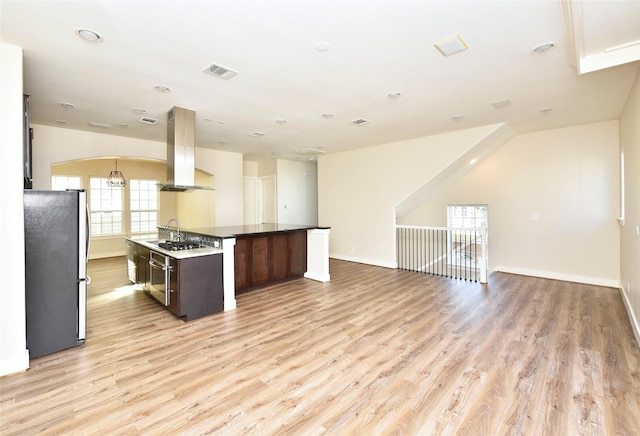 kitchen featuring dark brown cabinets, an island with sink, island range hood, stainless steel refrigerator, and light wood-type flooring