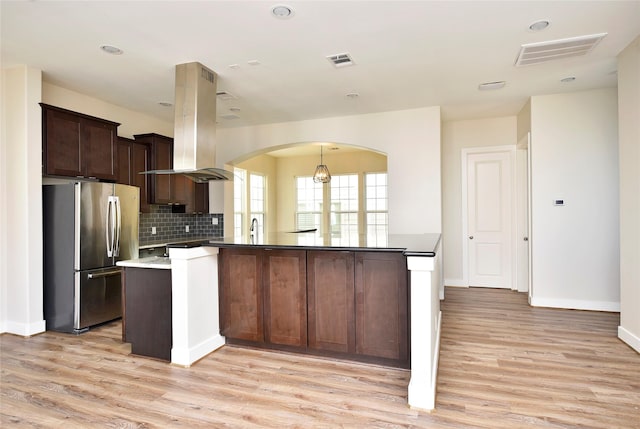 kitchen featuring island range hood, light hardwood / wood-style floors, stainless steel fridge, kitchen peninsula, and dark brown cabinets